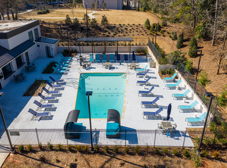 Cool down at this beautiful pool right in your community. Photo overlooking pool, pool chairs, loungers, and fence.